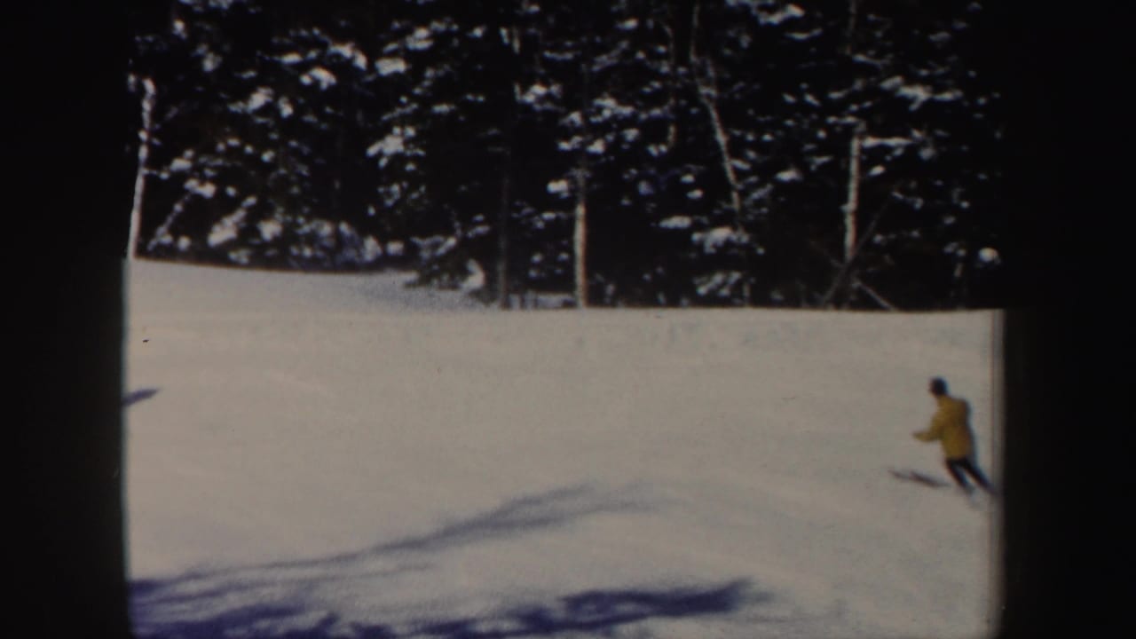 A distant skier in a yellow jacket descends a sunlit New Hampshire snow slope in this 1962 8mm frame.