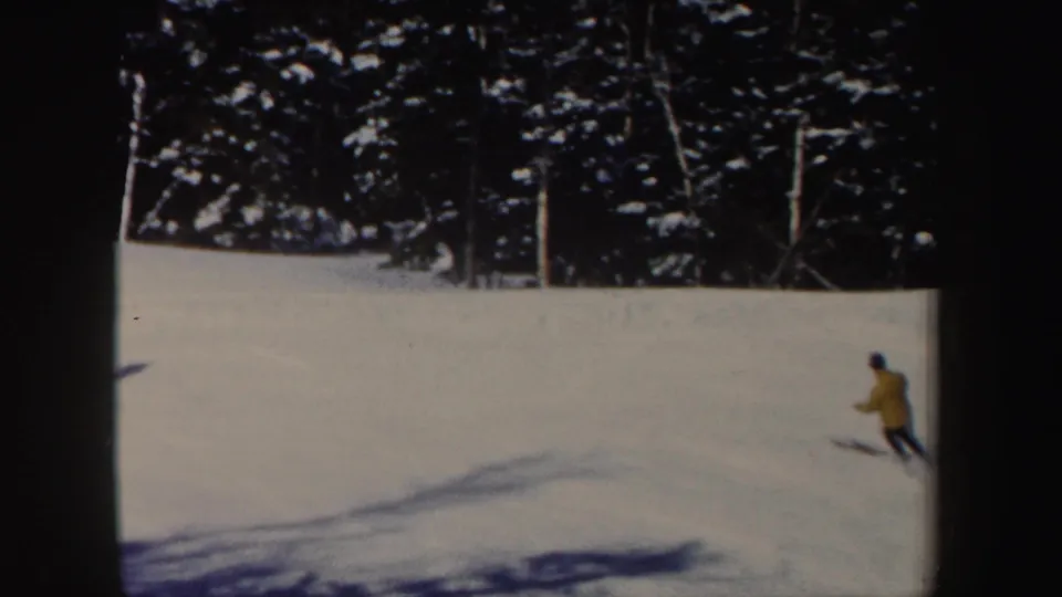 A distant skier in a yellow jacket descends a sunlit New Hampshire snow slope in this 1962 8mm frame.