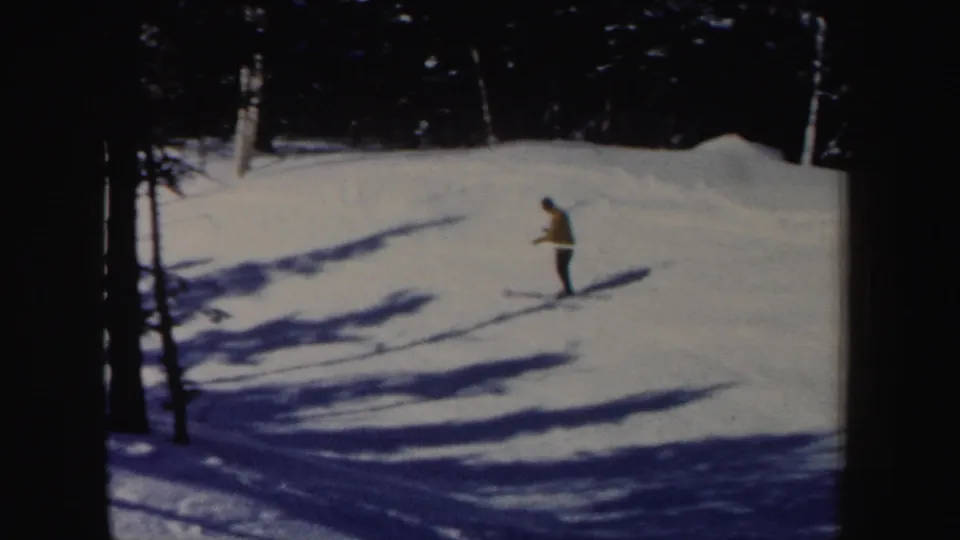 1962 New Hampshire 8mm frame with a yellow-jacket skier moving across a snowy incline under tree shadows.
