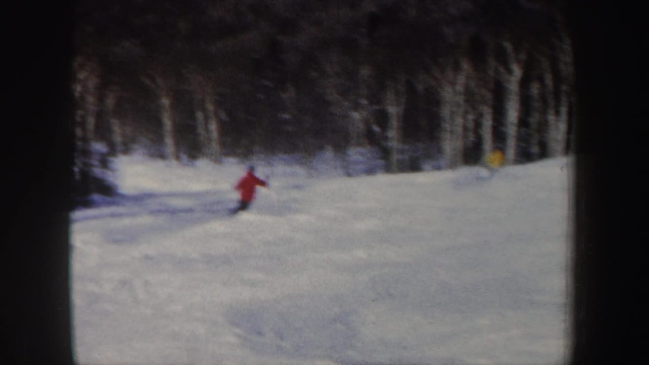 1962 New Hampshire home-movie frame showing a red-jacket skier on a snowy slope near a wooded edge.