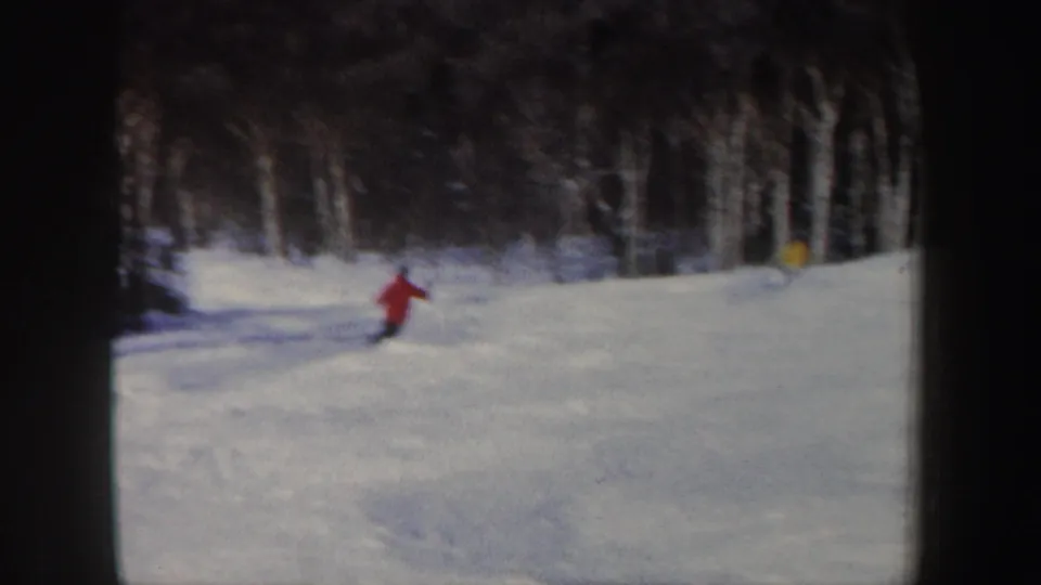 1962 New Hampshire home-movie frame showing a red-jacket skier on a snowy slope near a wooded edge.