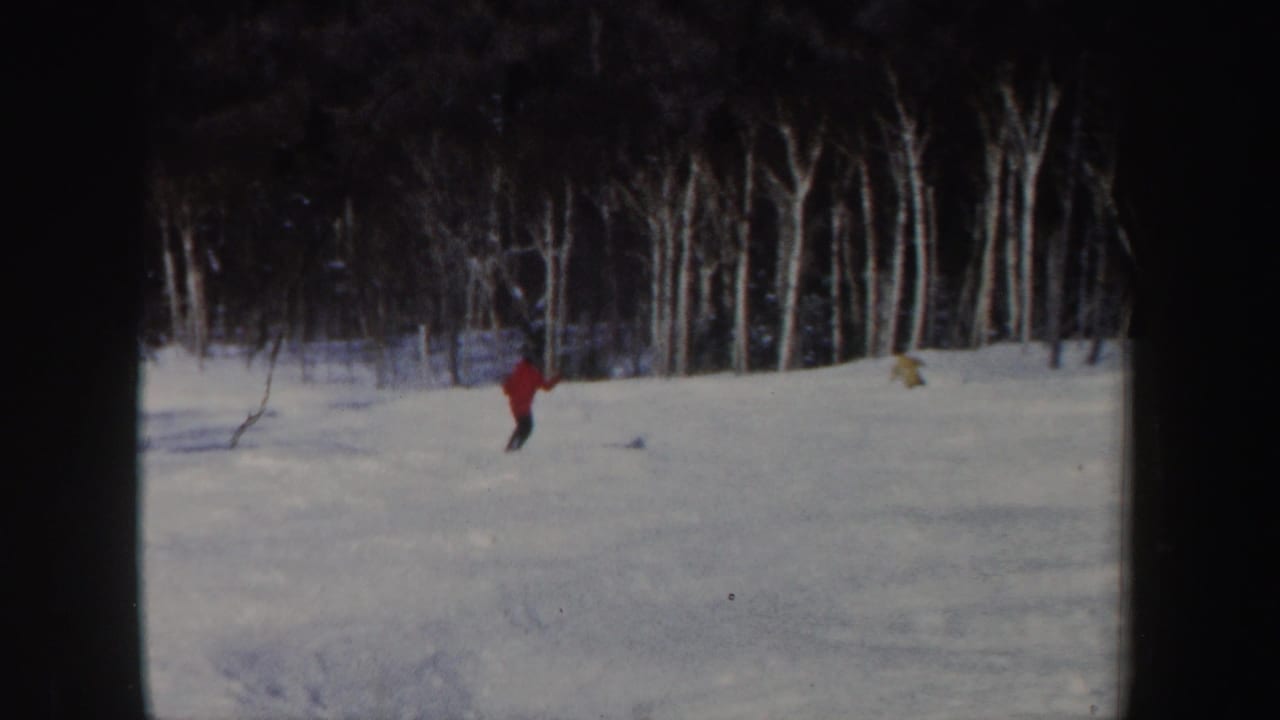1962 New Hampshire 8mm frame with a distant red-jacket skier crossing a broad snowy area before bare trees.
