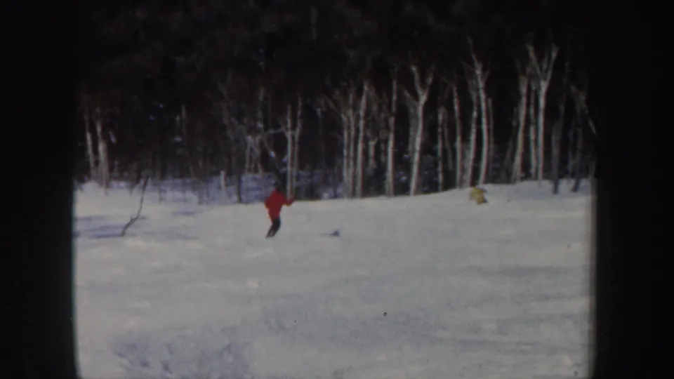 1962 New Hampshire 8mm frame with a distant red-jacket skier crossing a broad snowy area before bare trees.