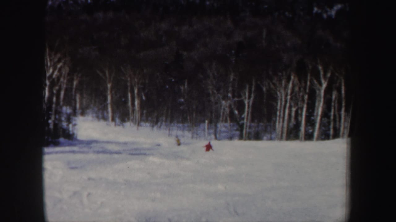 Distant red and yellow skiers cross a snowy New Hampshire slope in soft 1962 8mm footage.
