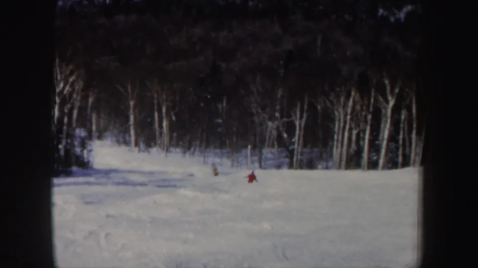 Distant red and yellow skiers cross a snowy New Hampshire slope in soft 1962 8mm footage.