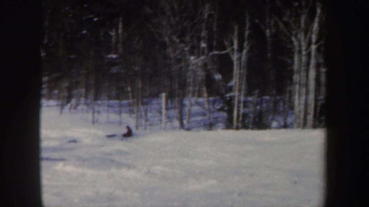 1962 New Hampshire 8mm frame showing a distant skier low on the snow near the edge of a bare winter forest.