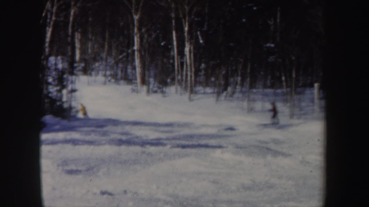 1962 New Hampshire home-movie frame showing a snowy wooded slope with distant skiers moving downhill.