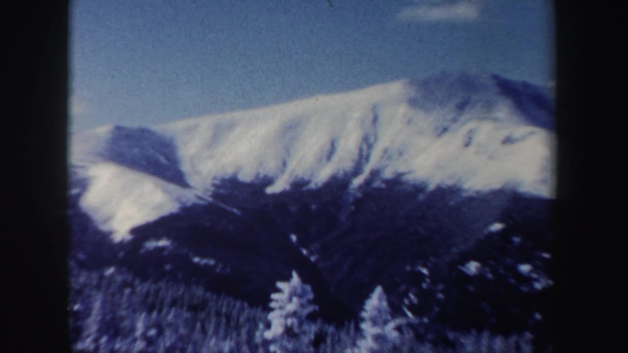 1962 New Hampshire mountain view with snow-covered peaks, blue sky, and dark forest below.