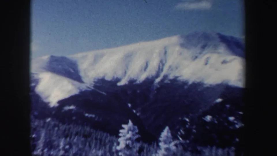 1962 New Hampshire mountain view with snow-covered peaks, blue sky, and dark forest below.