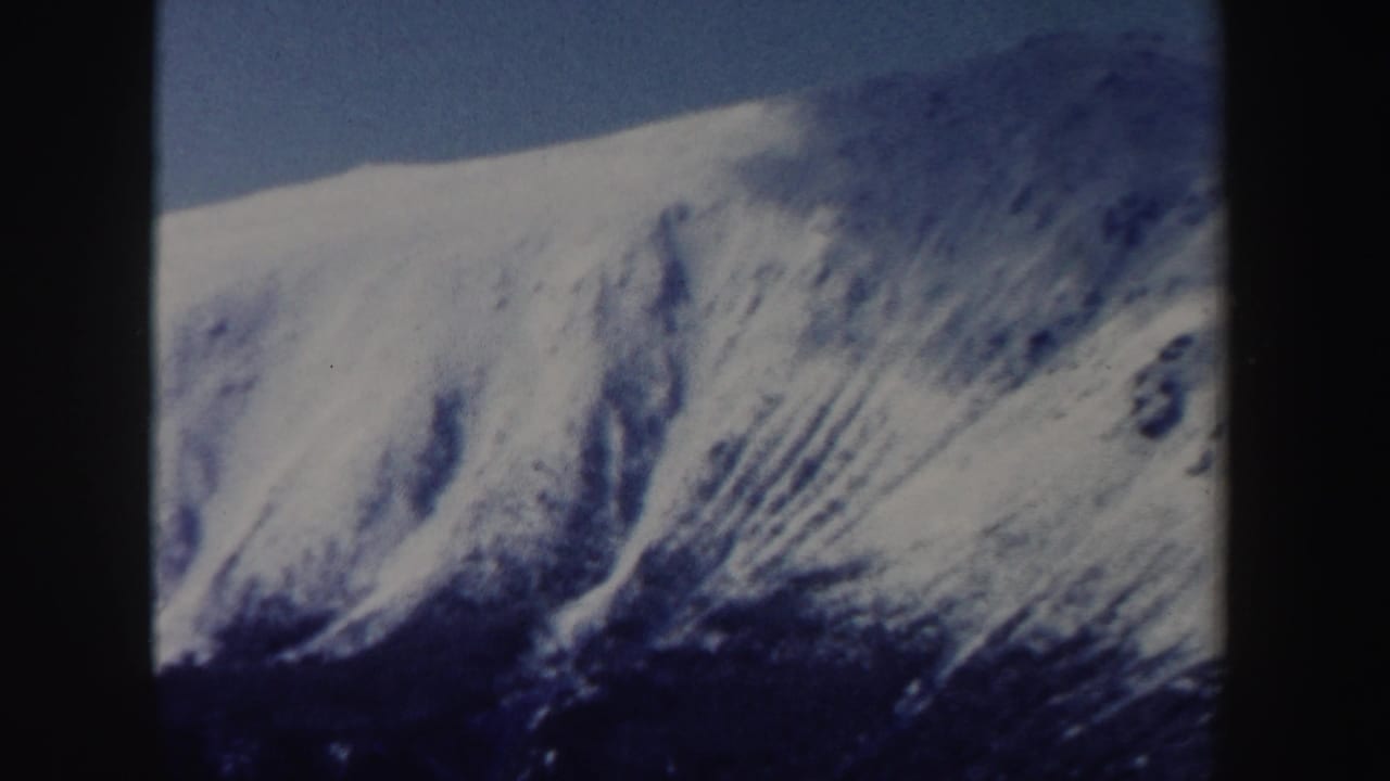 1962 New Hampshire 8mm frame showing a broad snow-covered mountain slope with shadowed texture under a blue sky.