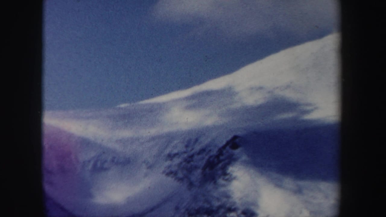 1962 New Hampshire 8mm frame with a snow-covered ridge, deep blue shadows, and blue sky, framed by the scanned film edge.