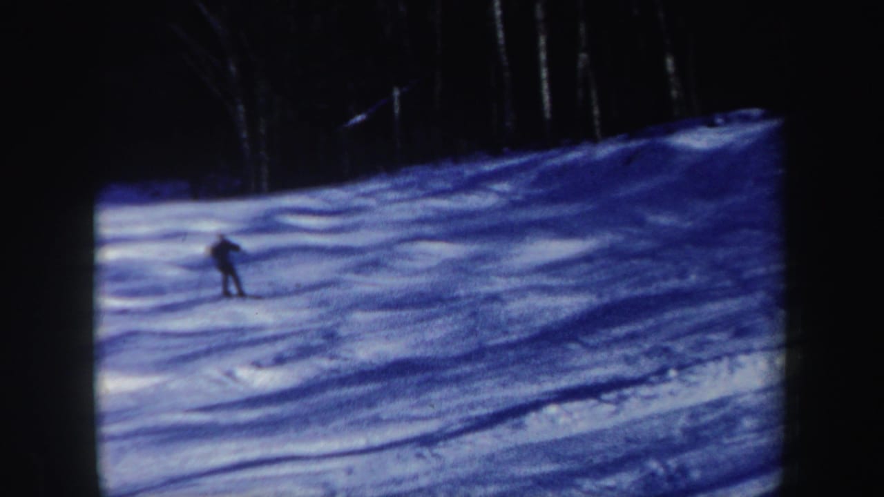 Distant skier on a New Hampshire snow slope, with trees and film grain visible in the 8mm frame.