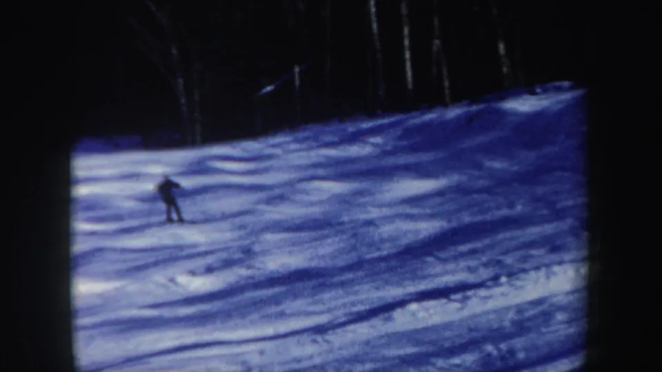 Distant skier on a New Hampshire snow slope, with trees and film grain visible in the 8mm frame.