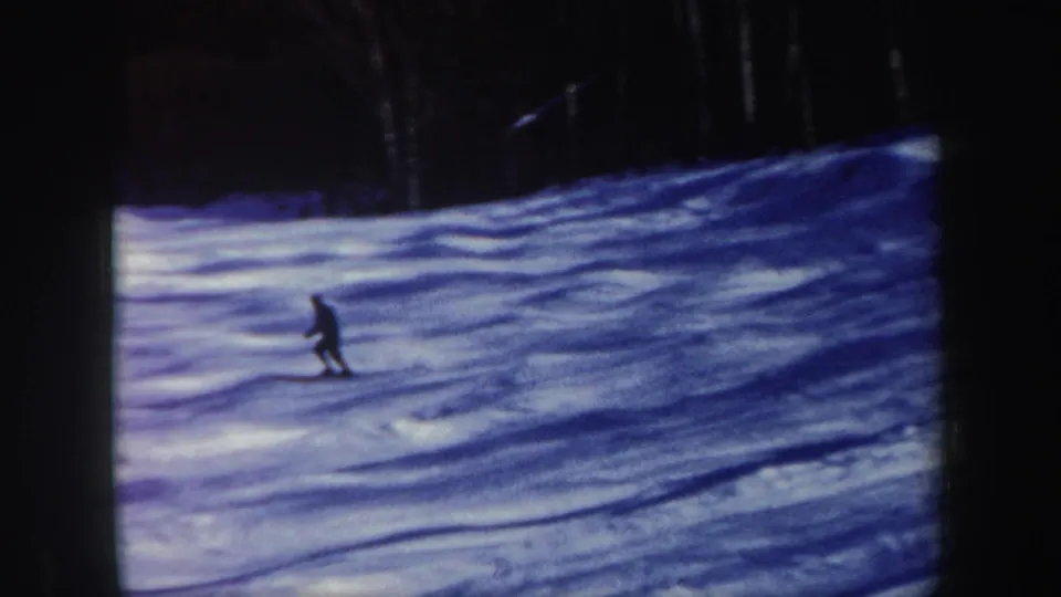 1962 New Hampshire home-movie frame of a lone skier gliding across a shadowed snowy slope.