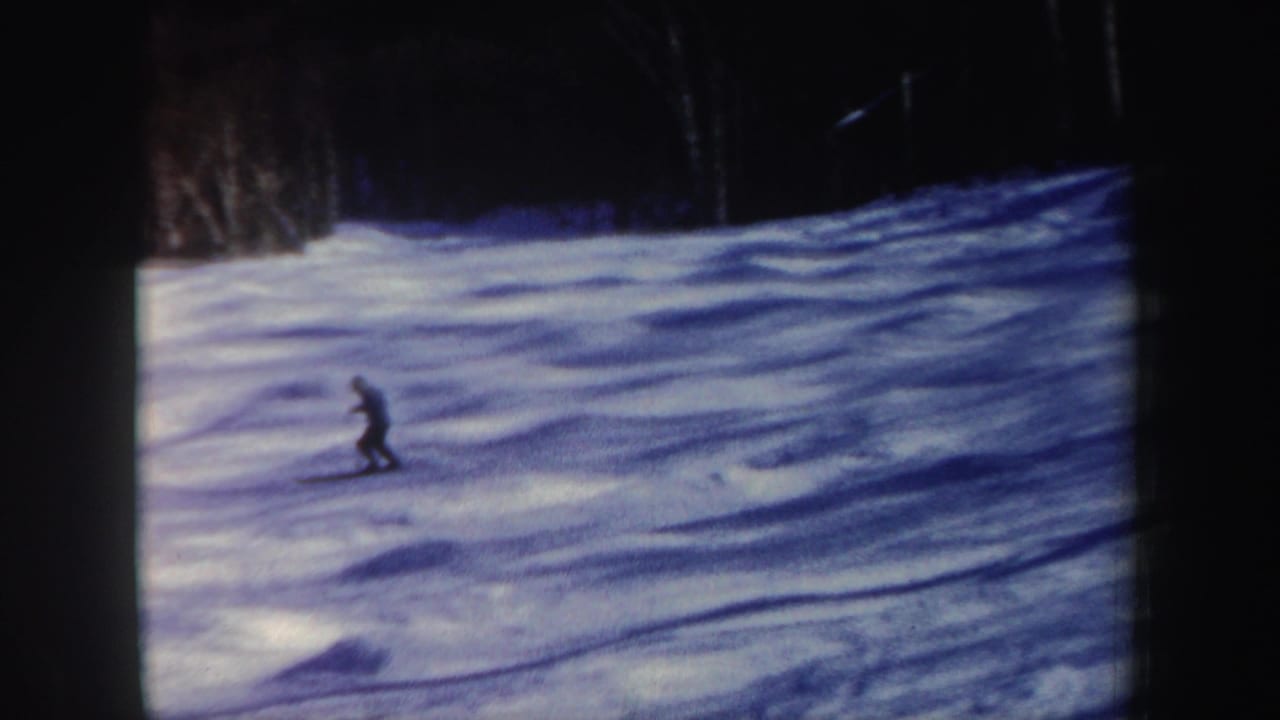 Lone skier crossing a snowy slope near a dark forest edge.