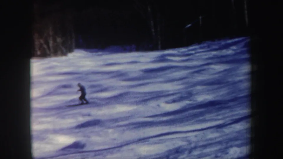 A distant skier in dark clothing moves across a blue-white snowy slope in 1962 New Hampshire home-movie footage.