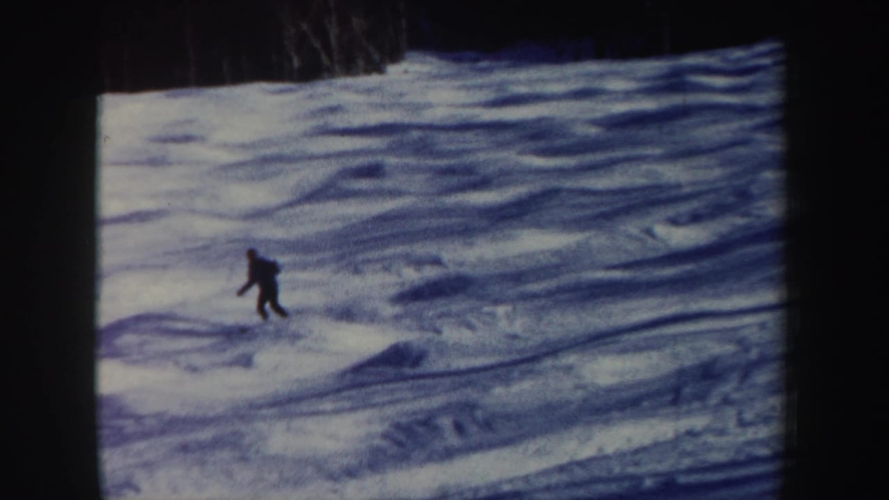 A distant skier in dark clothing bends into motion on a blue-toned snowy slope in the 1962 New Hampshire clip.