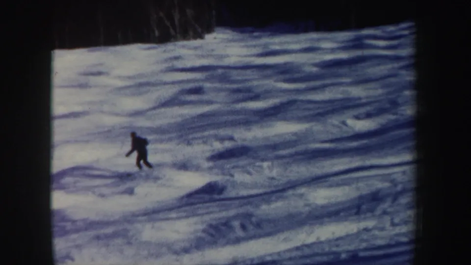 A distant skier in dark clothing bends into motion on a blue-toned snowy slope in the 1962 New Hampshire clip.