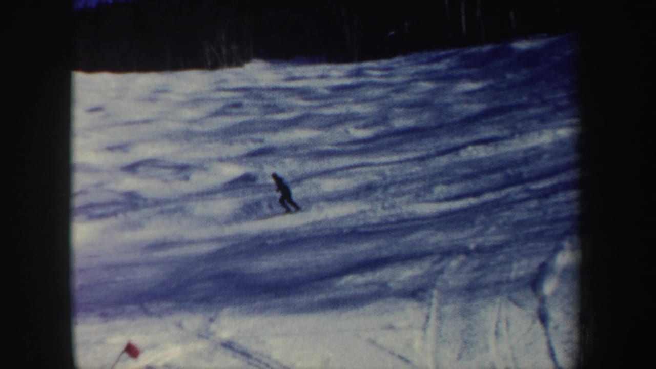 A distant skier approaches the lower slope, with a red course flag near the bottom of the 1962 New Hampshire frame.