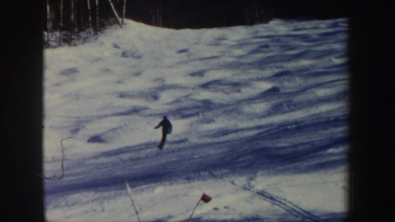 The skier moves toward the bottom of the New Hampshire slope, with red marker flags and blue snow shadows visible.
