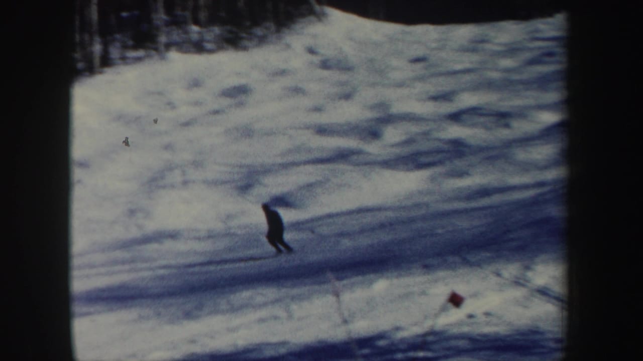 1962 New Hampshire 8mm frame showing a lone adult skier moving downhill across blue-tinted snow below a dark tree line.