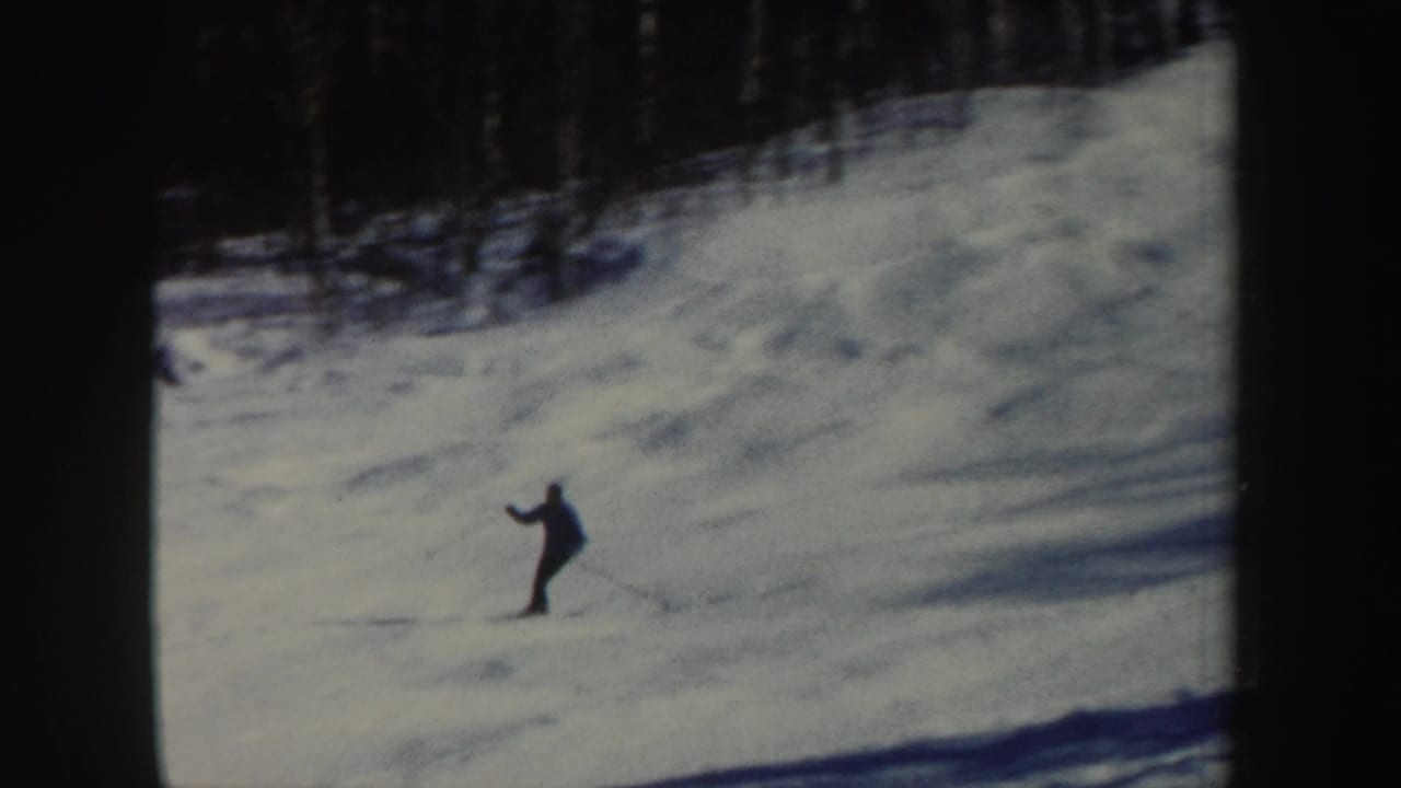 A lone skier appears mid-slope in New Hampshire home-movie footage, with wooded background and dark film borders.