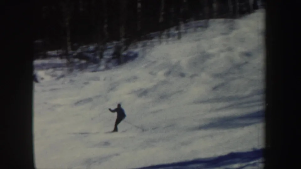 A lone skier appears mid-slope in New Hampshire home-movie footage, with wooded background and dark film borders.