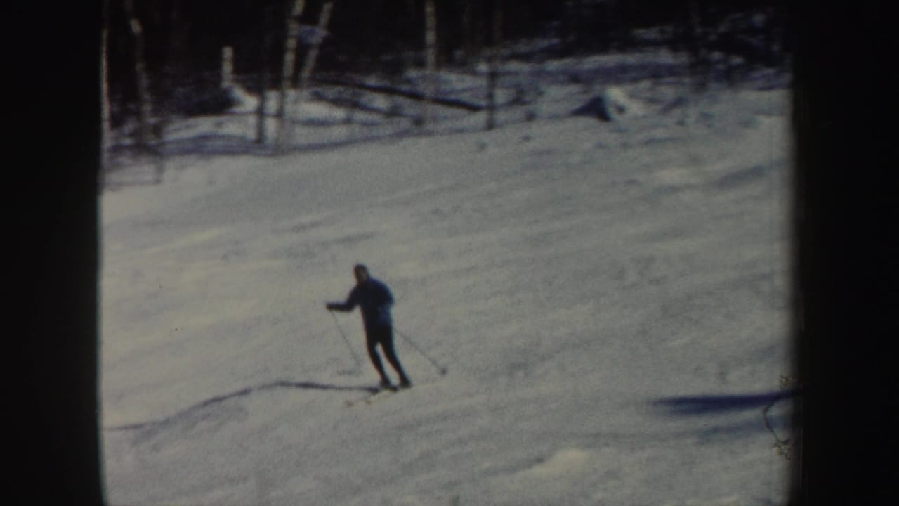 The adult skier is nearer the camera, leaning into the descent on a snow-covered New Hampshire slope in 8mm footage.