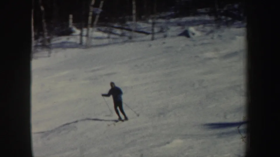 The adult skier is nearer the camera, leaning into the descent on a snow-covered New Hampshire slope in 8mm footage.