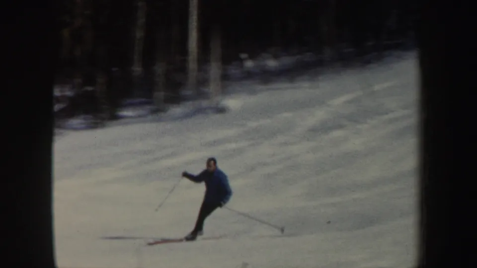 A closer 1962 home-movie frame shows the skier with poles extended, dark clothing, and blue-tinted snow across the slope.