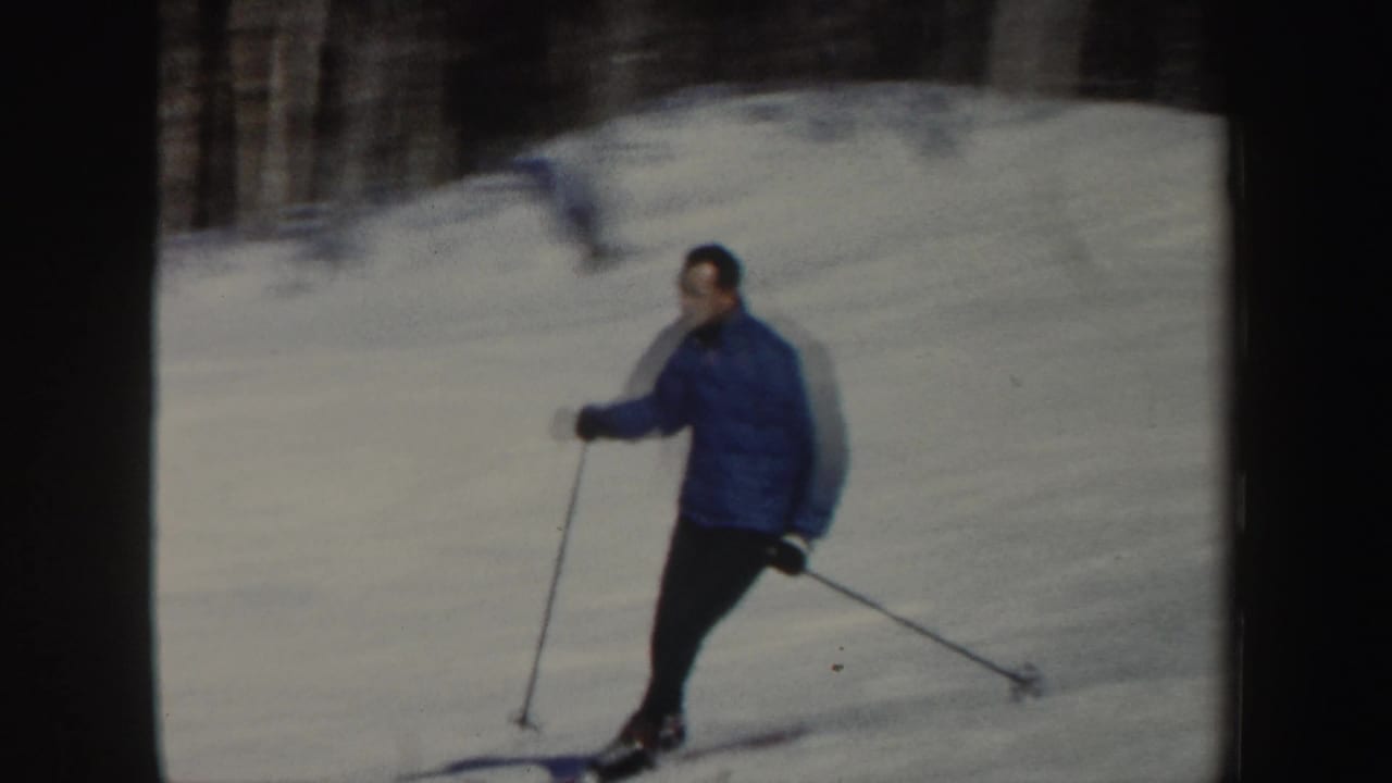 Adult skier in a blue jacket descends a snowy New Hampshire hillside, framed in soft 1962 8mm color.