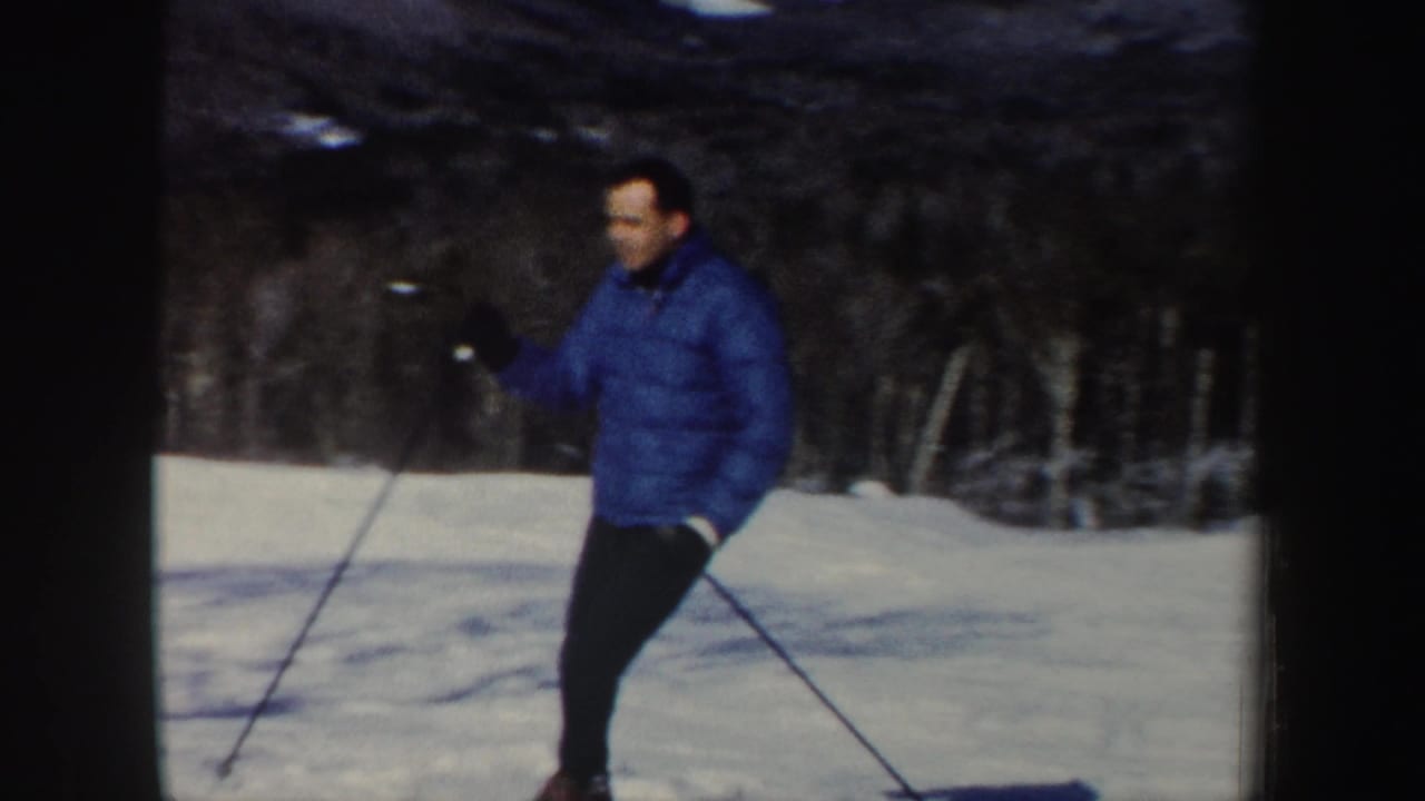 Closer 1962 home-movie frame of an adult skier in a blue jacket passing the camera on a snowy New Hampshire slope.