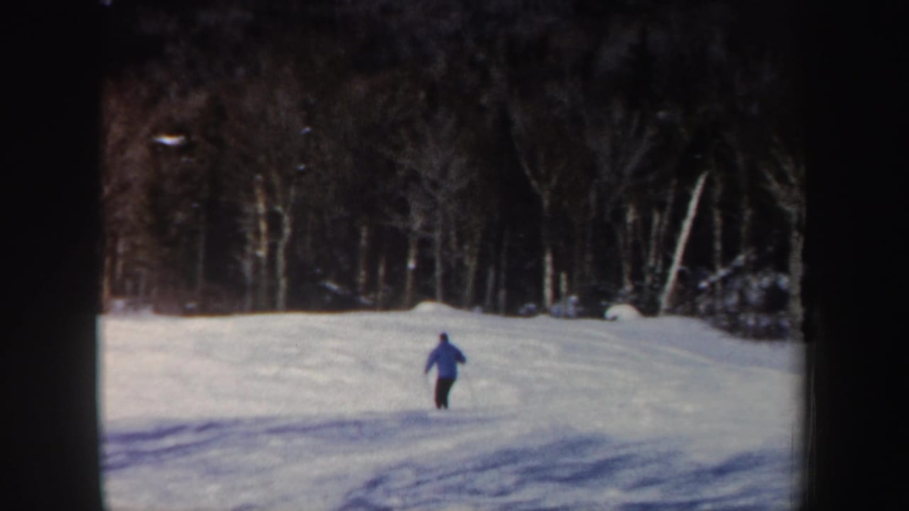 Distant view of the adult skier continuing downhill across a snowy New Hampshire slope in 1962 8mm footage.