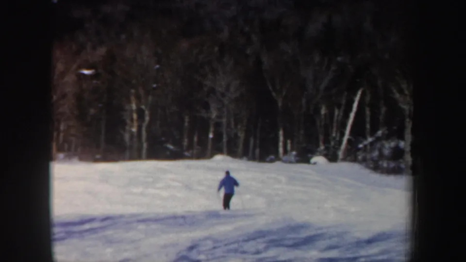 Distant view of the adult skier continuing downhill across a snowy New Hampshire slope in 1962 8mm footage.