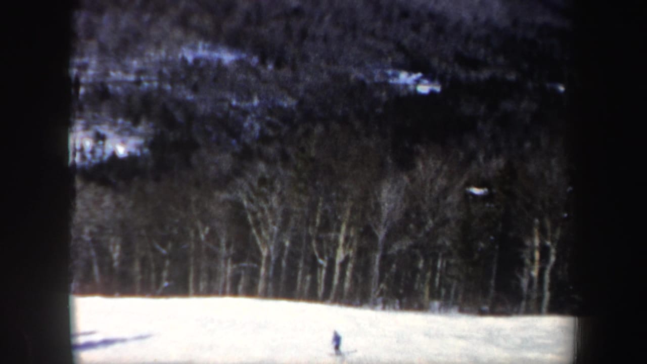 1962 New Hampshire 8mm frame of a distant skier on a snow-covered slope beneath bare winter trees.