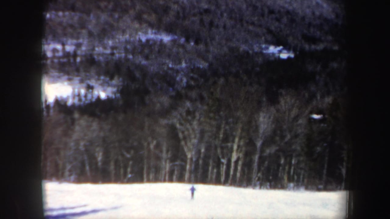 A small skier moves across a New Hampshire snowfield, framed by dark woods in soft 8mm color.
