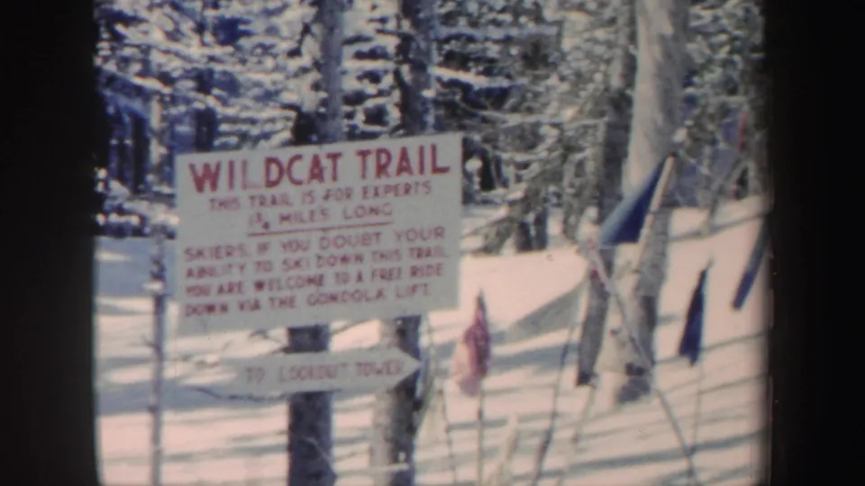 1962 New Hampshire 8mm frame showing a Wildcat Trail expert-ski warning sign among snow-covered trees and trail flags.