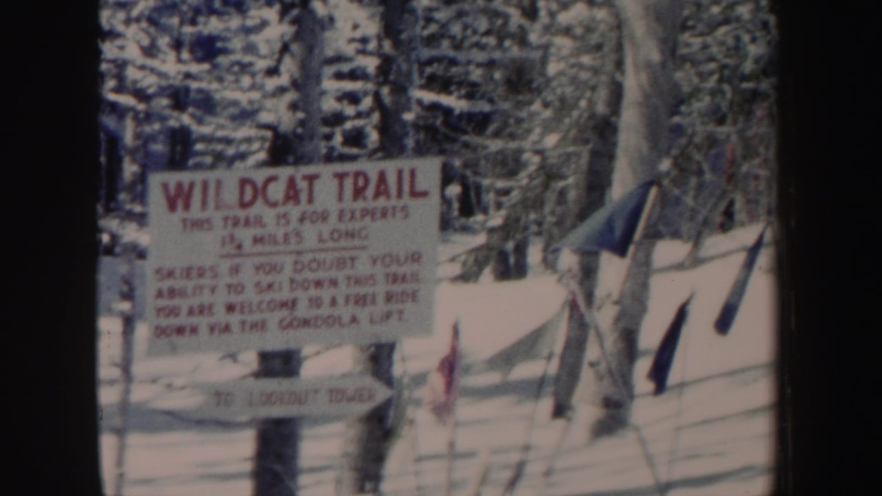 1962 New Hampshire home-movie frame holding on a Wildcat Trail sign in a snow-covered conifer forest.