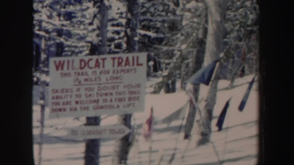 1962 New Hampshire home-movie frame holding on a Wildcat Trail sign in a snow-covered conifer forest.