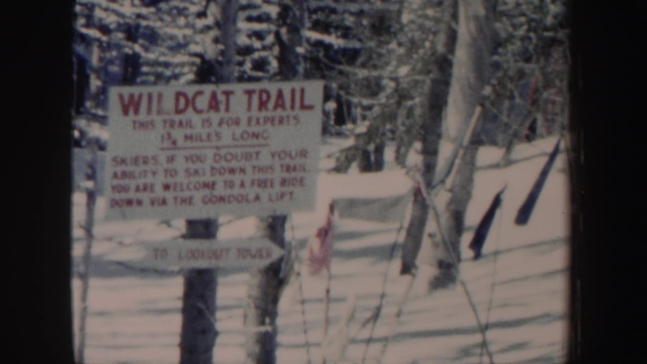 1962 New Hampshire 8mm frame of the Wildcat Trail expert warning sign, set against snowy woods with a small red flag and fencing lines.