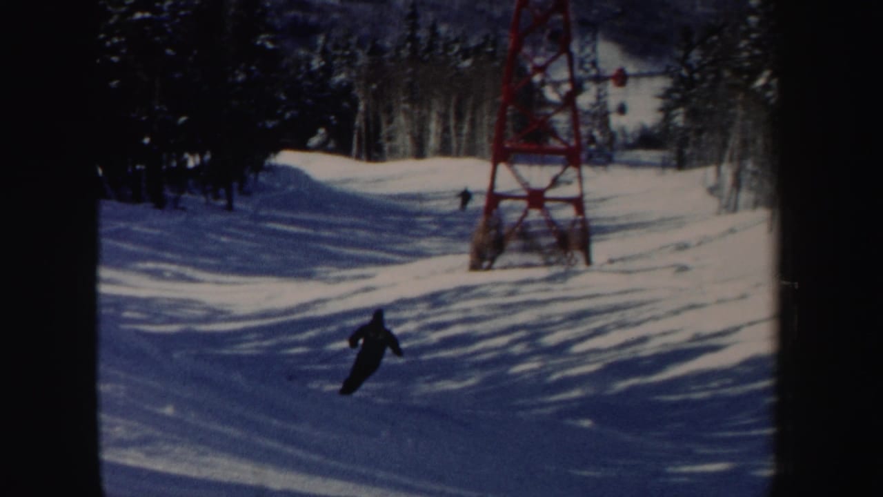 Skier descending a snowy slope near a red ski lift tower and evergreen trees.