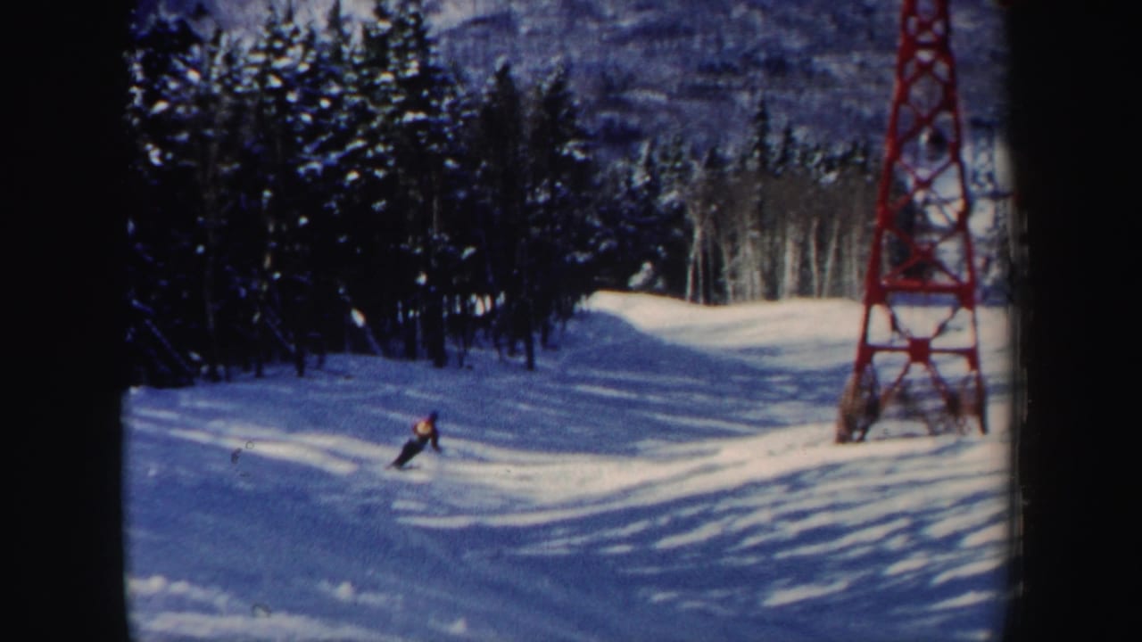 The skier appears farther across the groomed New Hampshire run, with woods, shadows, and the red tower framing the scene.