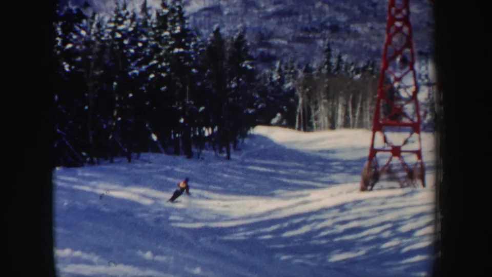 The skier appears farther across the groomed New Hampshire run, with woods, shadows, and the red tower framing the scene.