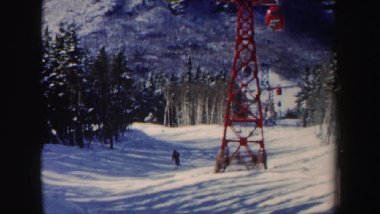 1962 New Hampshire ski slope with a red lift tower and a distant skier moving between snow-covered trees.