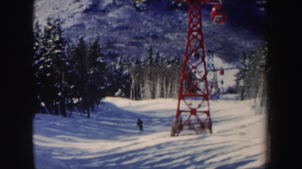 1962 New Hampshire ski slope with a red lift tower and a distant skier moving between snow-covered trees.