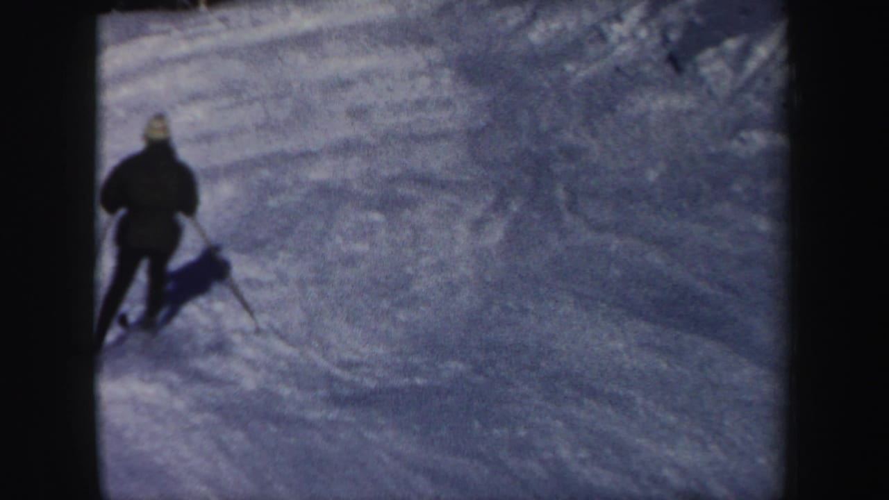 Rear view of a skier descending a shaded New Hampshire ski run, filmed in soft 1962 8mm color.