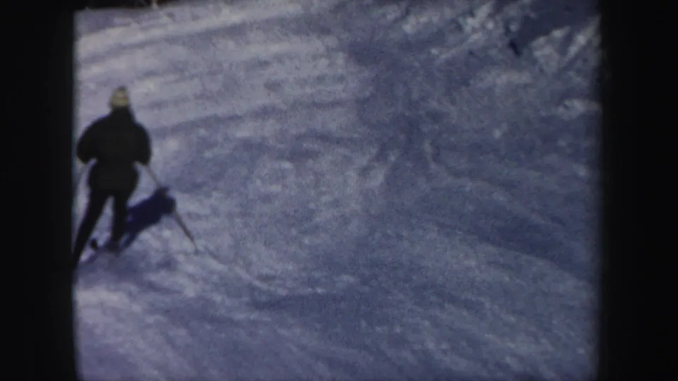 Rear view of a skier descending a shaded New Hampshire ski run, filmed in soft 1962 8mm color.