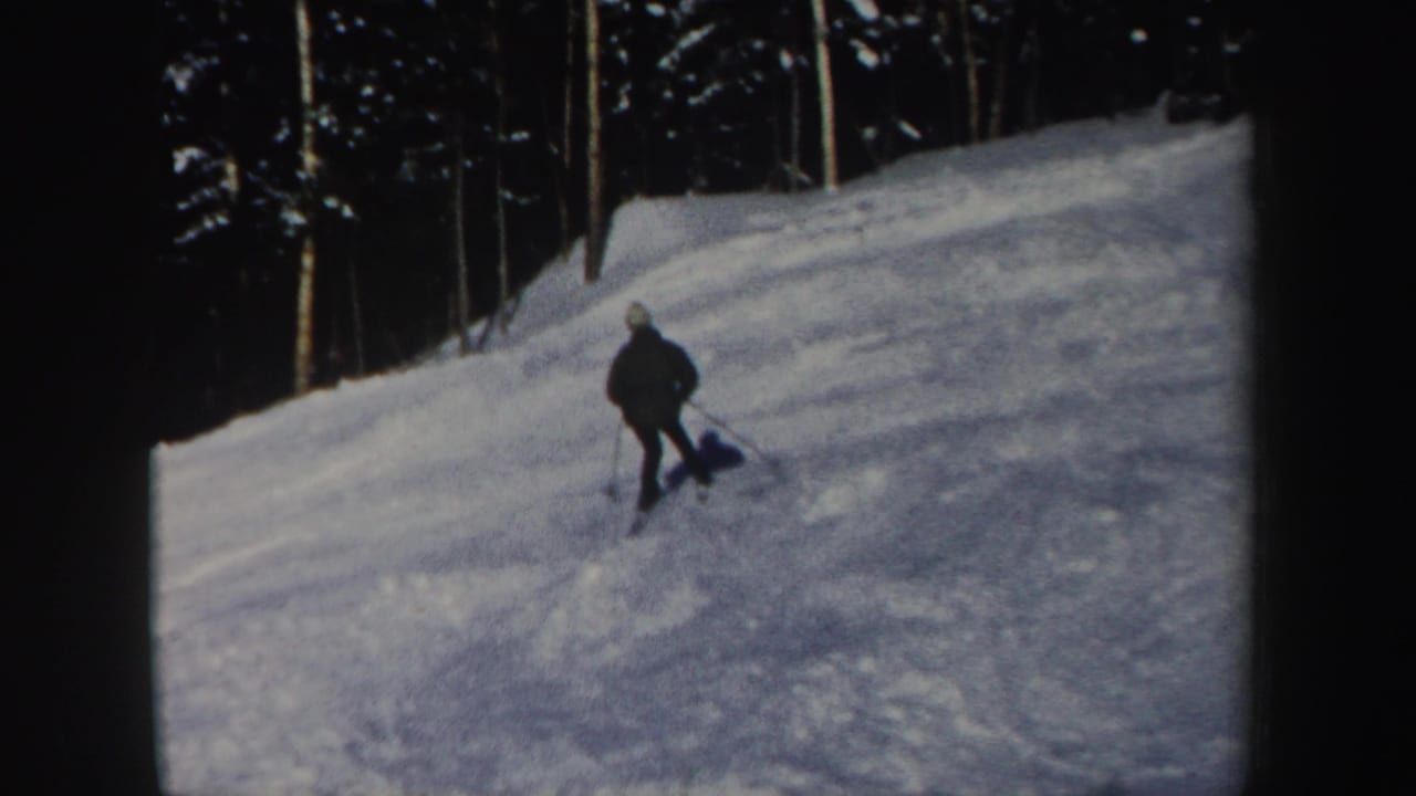 A lone skier in dark winter clothing descends a snowy New Hampshire forest slope in 1962 home-movie footage.