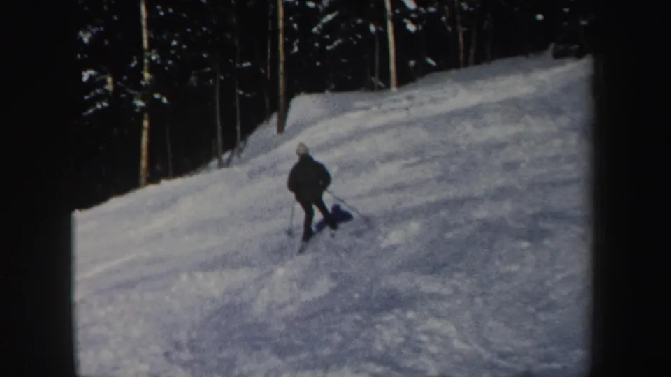 A lone skier in dark winter clothing descends a snowy New Hampshire forest slope in 1962 home-movie footage.