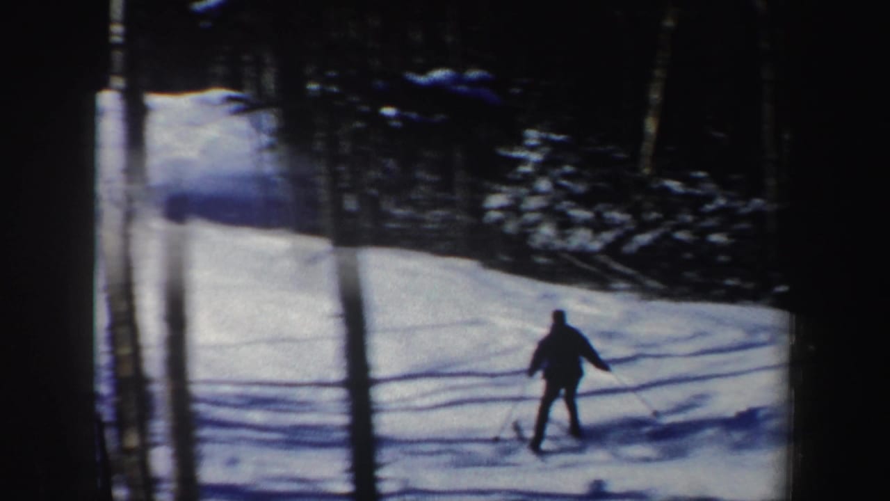 A skier descends through a wooded New Hampshire snow slope, seen from a home-movie camera behind trees in 1962.